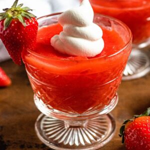 Strawberry kissel in a glass with a whole strawberry on the side with a dollop of cream on top.