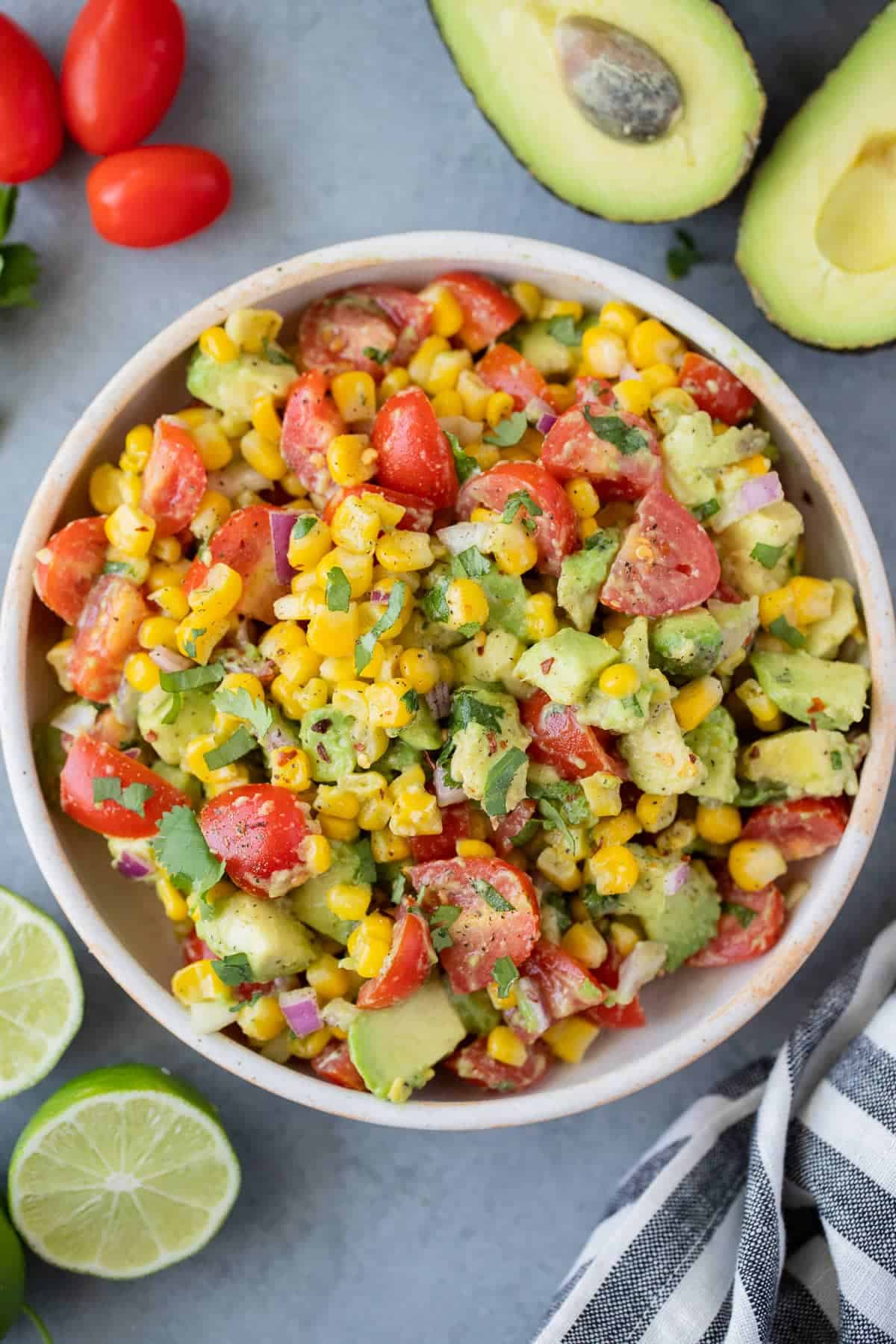 Corn tomato avocado salad in a bowl with halved limes on the side. 