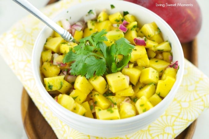 Bowl of mango salad with a cilantro sprig on top with a spoon tucked in. 
