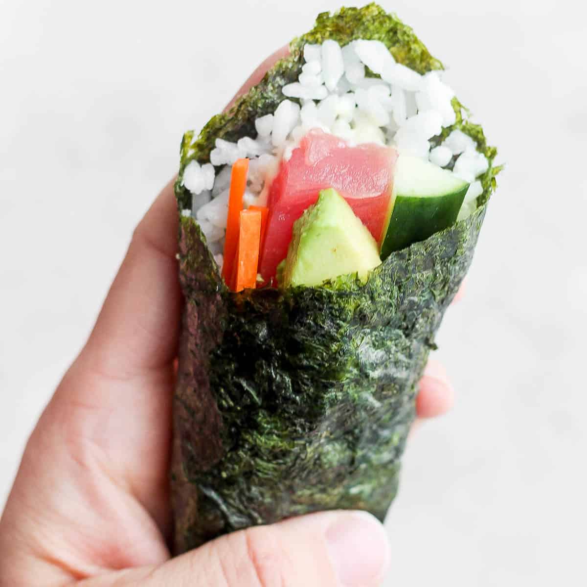 Hand holding up a sushi hand roll. 