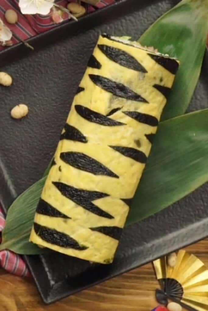 A complete tiger roll sitting a top a green leaf on a black matte serving platter. 