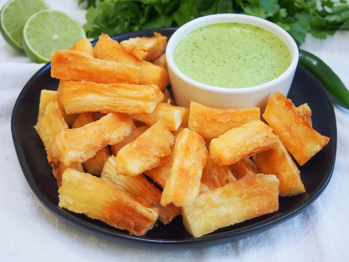 Yuca fries served on a small black plate with a side of dipping sauce. 