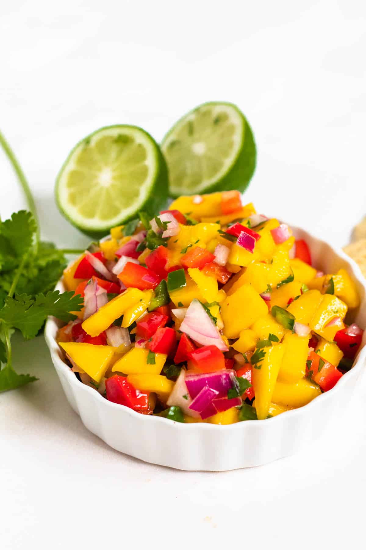 Small dish with mango pico de gallo sitting in front of halved limes and cinlantro sprigs. 