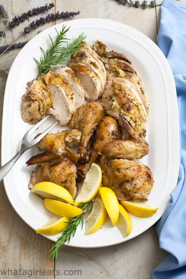 French roasted chicken cut into slices along with wings and drumsticks and served on a platter with lemon wedges on the edge. 