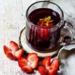 A glass of hibiscus tea with strawberries decorated like flowers next to them.