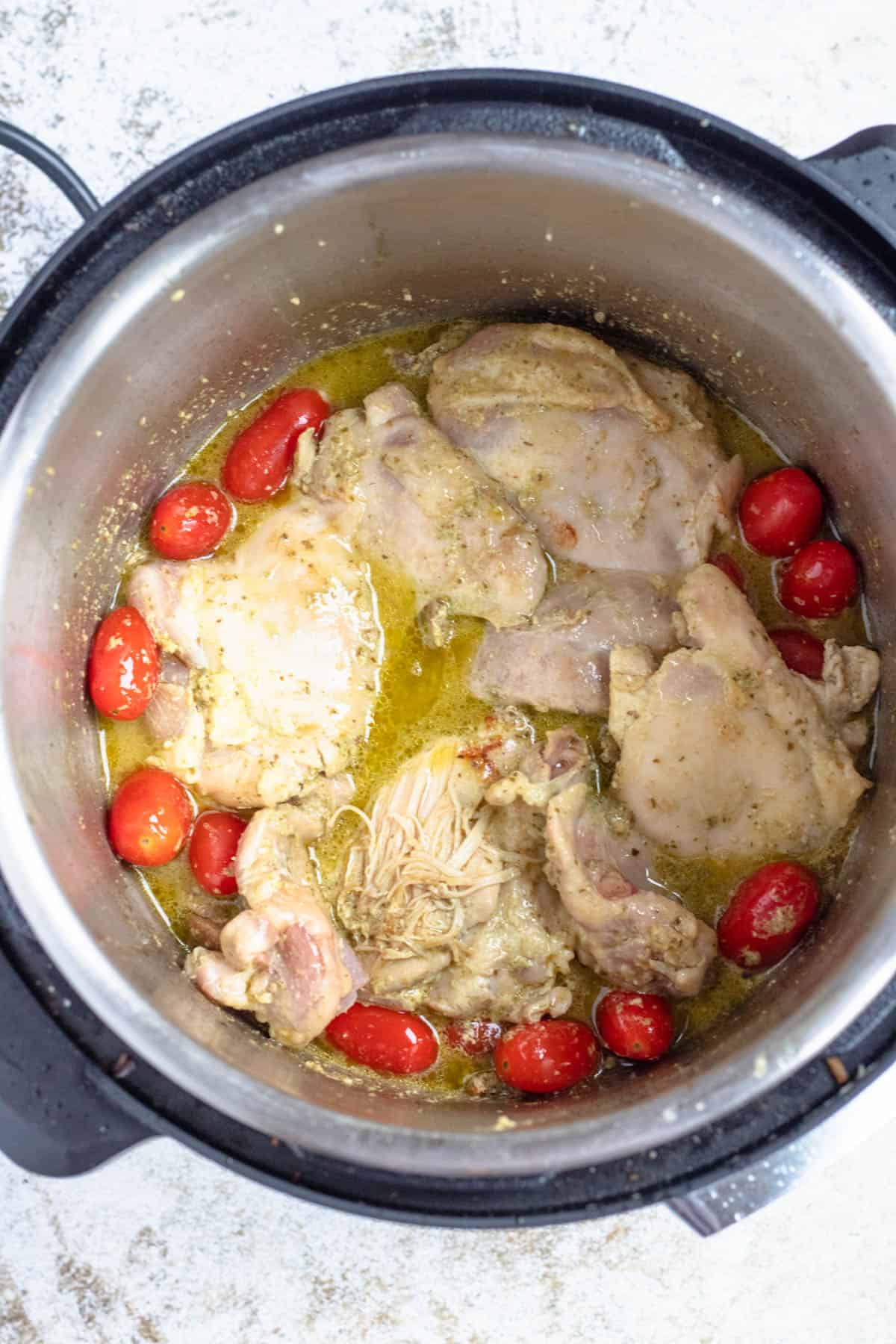 Chicken thighs added into the instant pot with broth and tomatoes, ready to cook. 