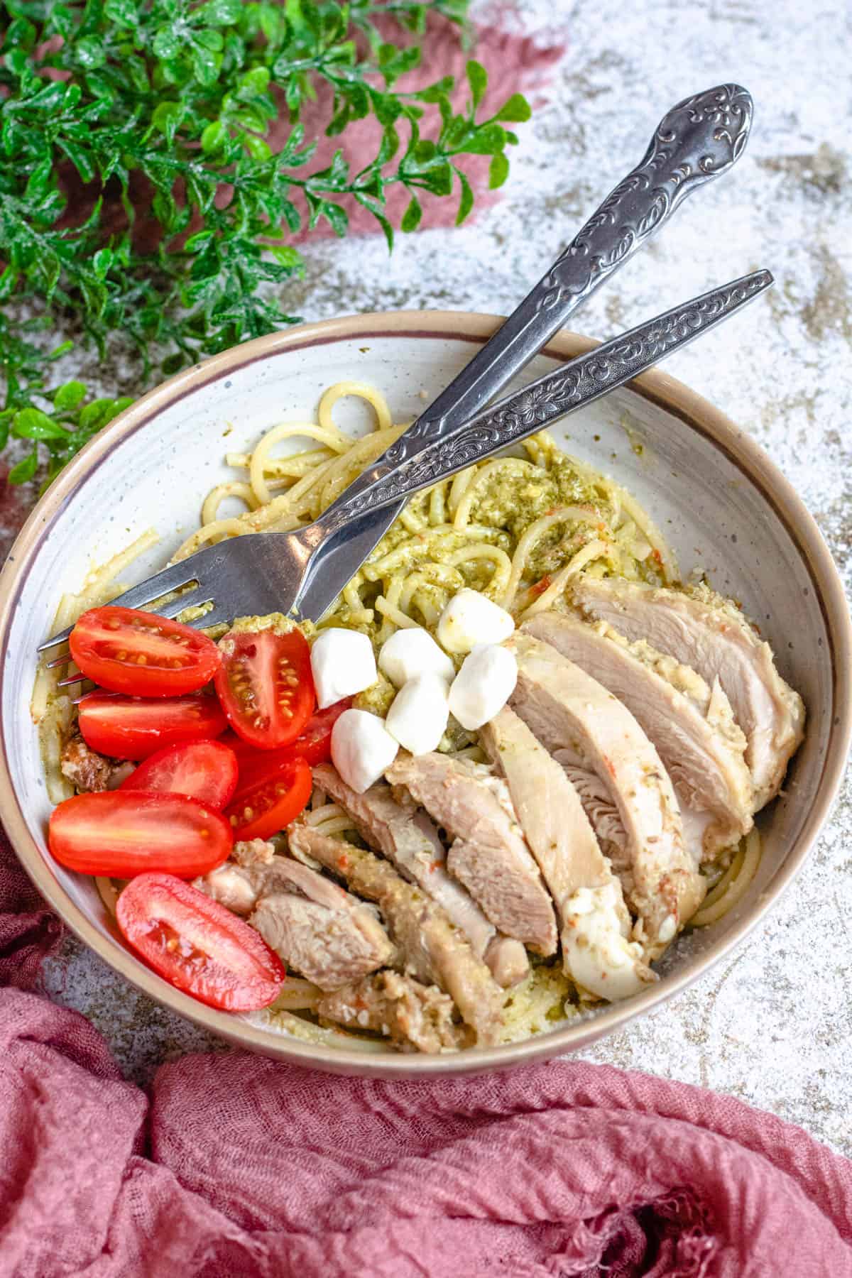 Pasta bowl filled with instant pot pesto chicken, fresh grape tomatoes sliced in half and some fresh mozzarella balls served over it. 