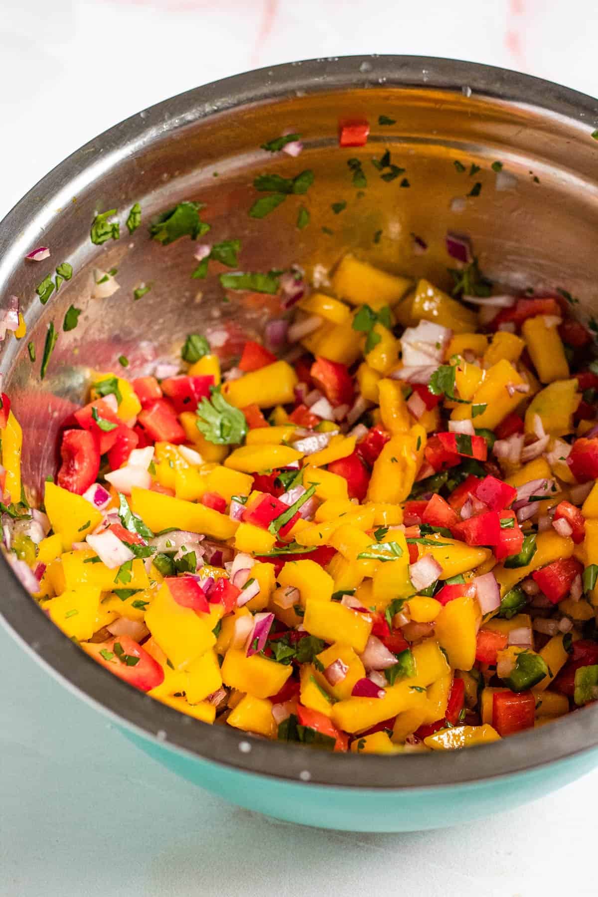 Ingredients combined in a mixing bowl to make mango pico de gallo. 
