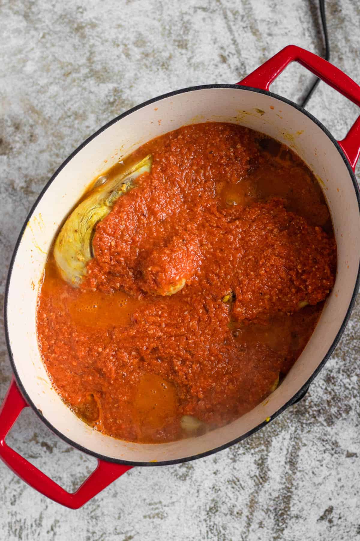 Chicken in a dutch oven covered in seasoned tomato sauce for the meat in pan con pollo. 