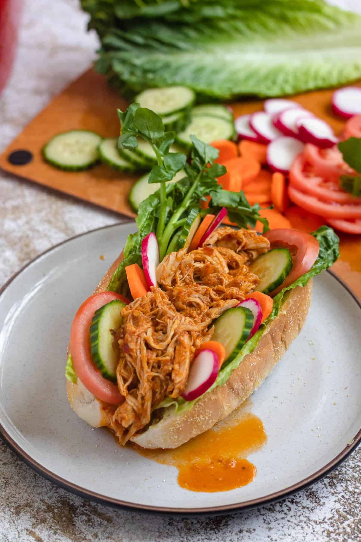pan con pollo on a plate topped with lettuce and other fresh veggies sitting in front of the cutting board with remaining toppings. 