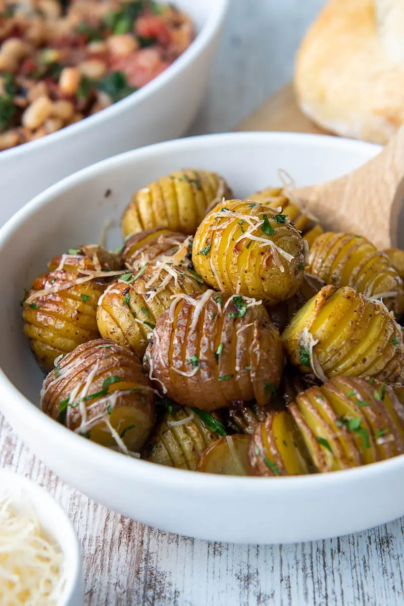 Wooden spoon tucked into a bowl of mini hasselback potatoes. 