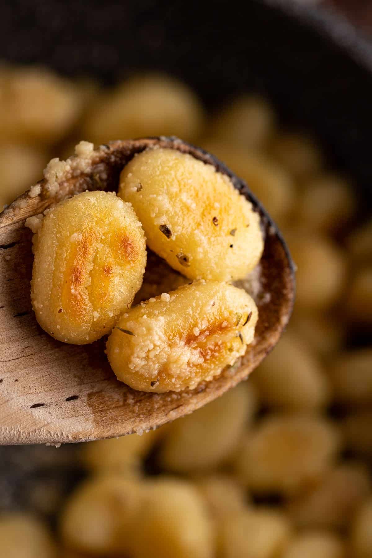 Crispy pan fried gnocchi sitting on a wooden spoon. 