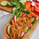 Pinterest image of Pan con Pollo on a plate, topped with lettuce and other fresh veggies, sitting in front of the cutting board with remaining toppings.