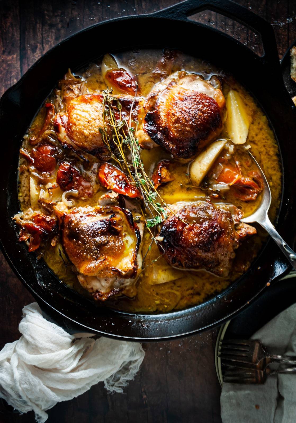 Vinegar braised chicken sitting in sauce in a cast iron pan. 