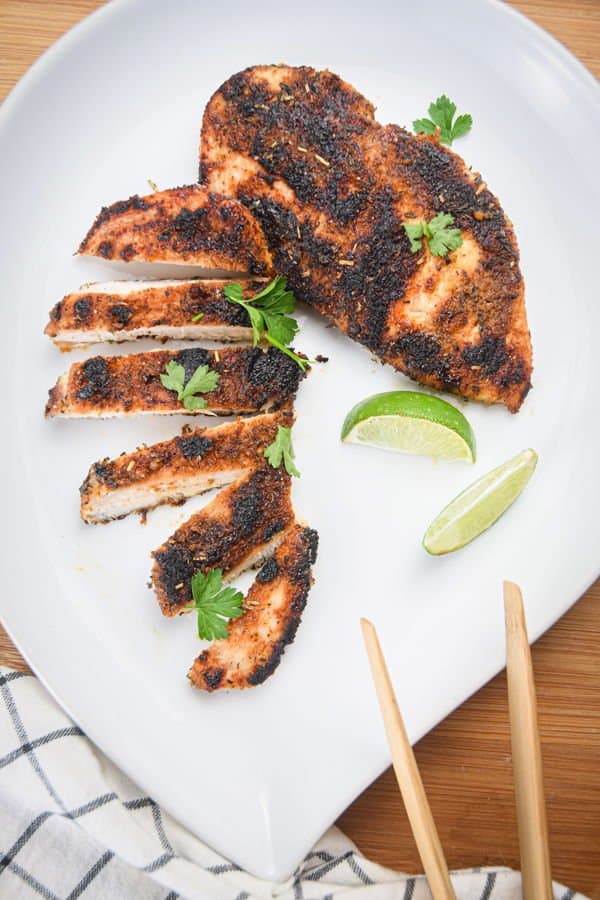 Blackened chicken sliced into strips on a plate with lime wedges sitting next to it. 