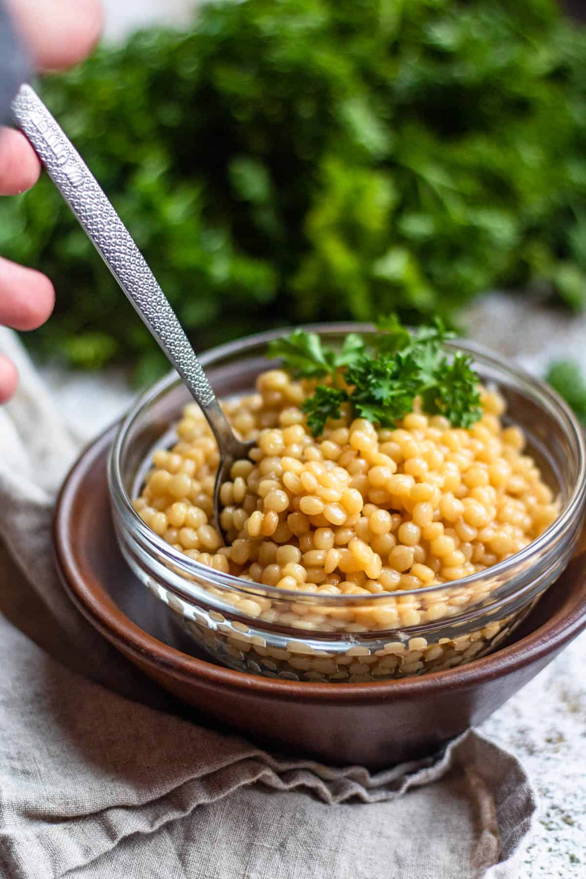 Bowlful of Instant Pot Israeli Couscous with a hand tucking a spoon into it. 