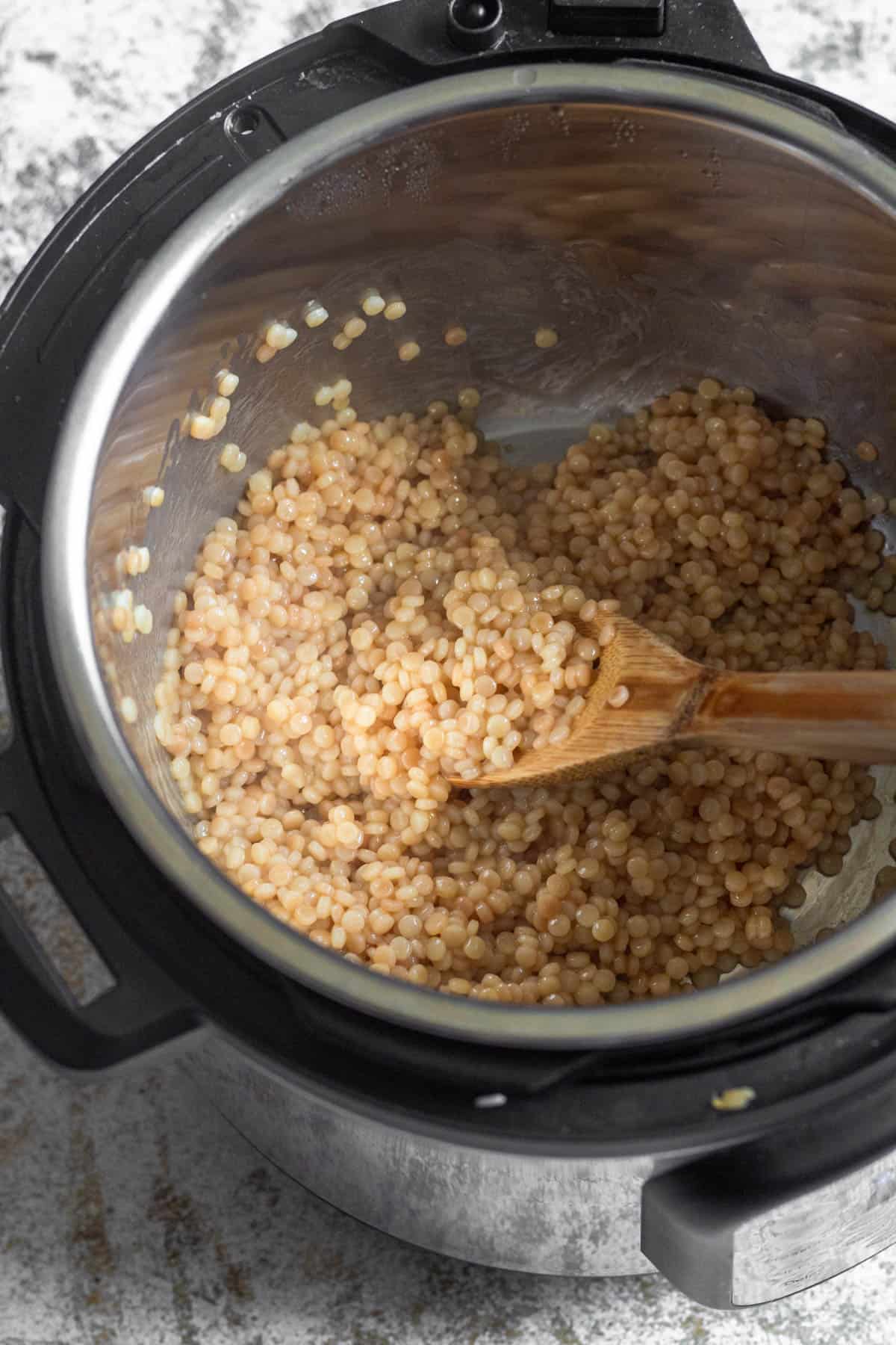 Cooked Instant Pot Israeli Couscous with a wooden spoon stirring it up. 