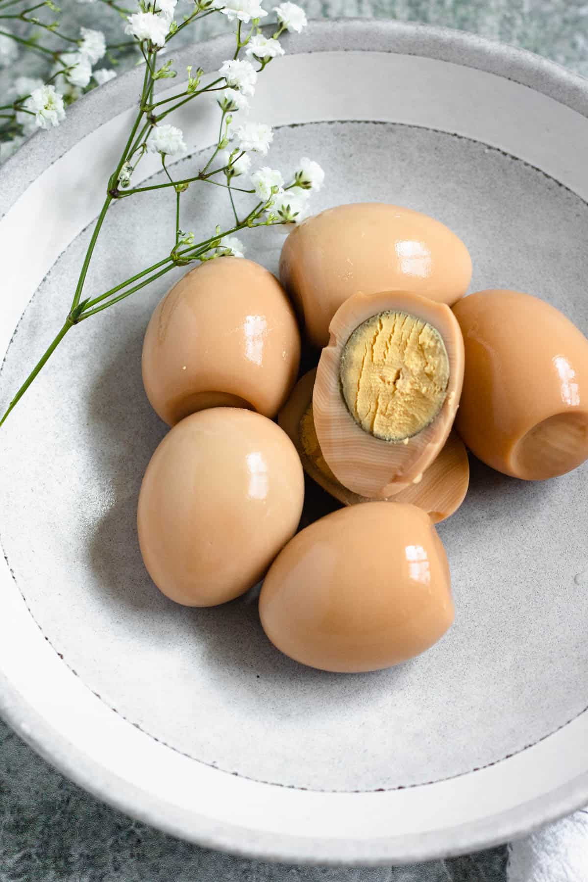 Hard boiled eggs with the whites dyed brown on a plate with a floral garnish. 