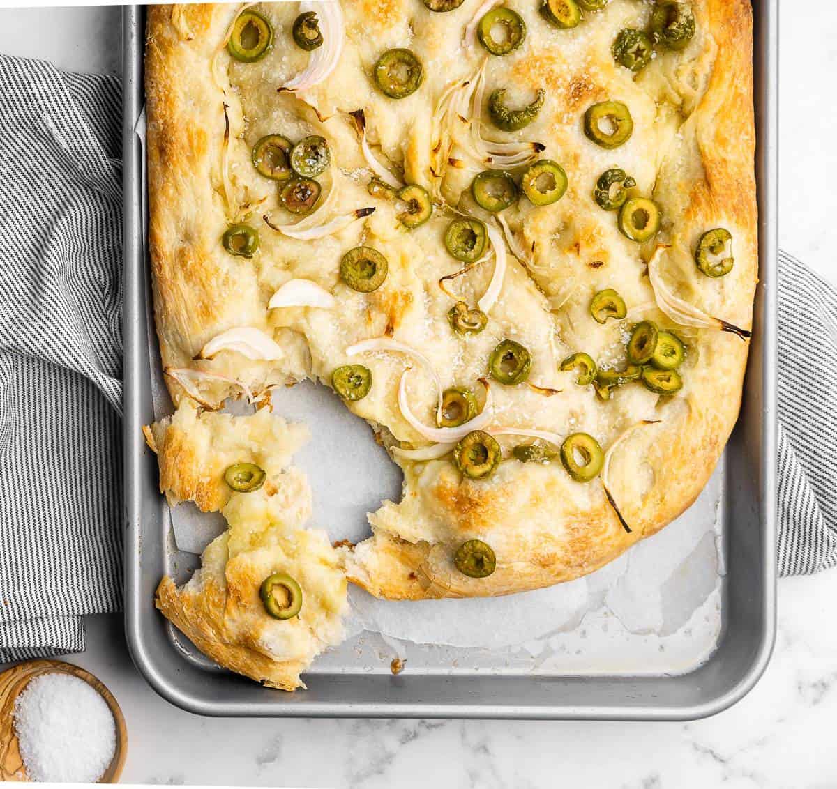 Olive and onion focaccia bread laying in a baking pan. 
