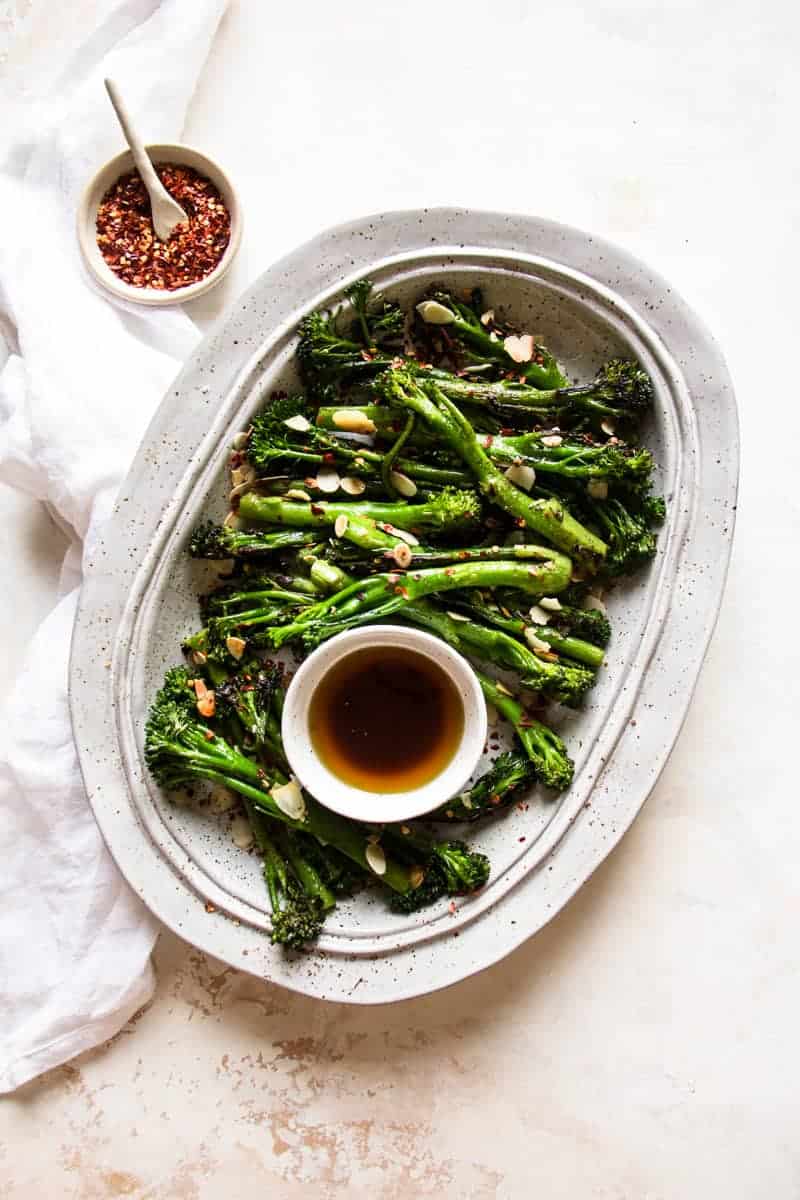 Rectangular serving plate with broccolini and an small dish with asian marinade beside it. | Cooking with Elo