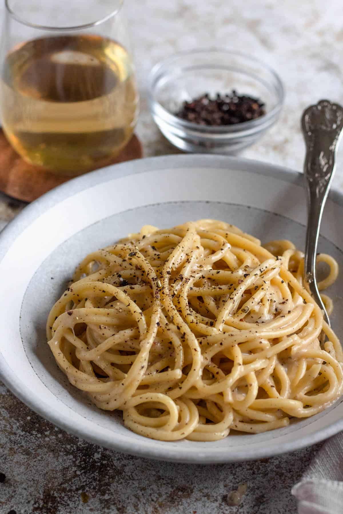 Bowl of bucatini cacio e pepe with freshly cracked pepper over it and a fork tucked in. 