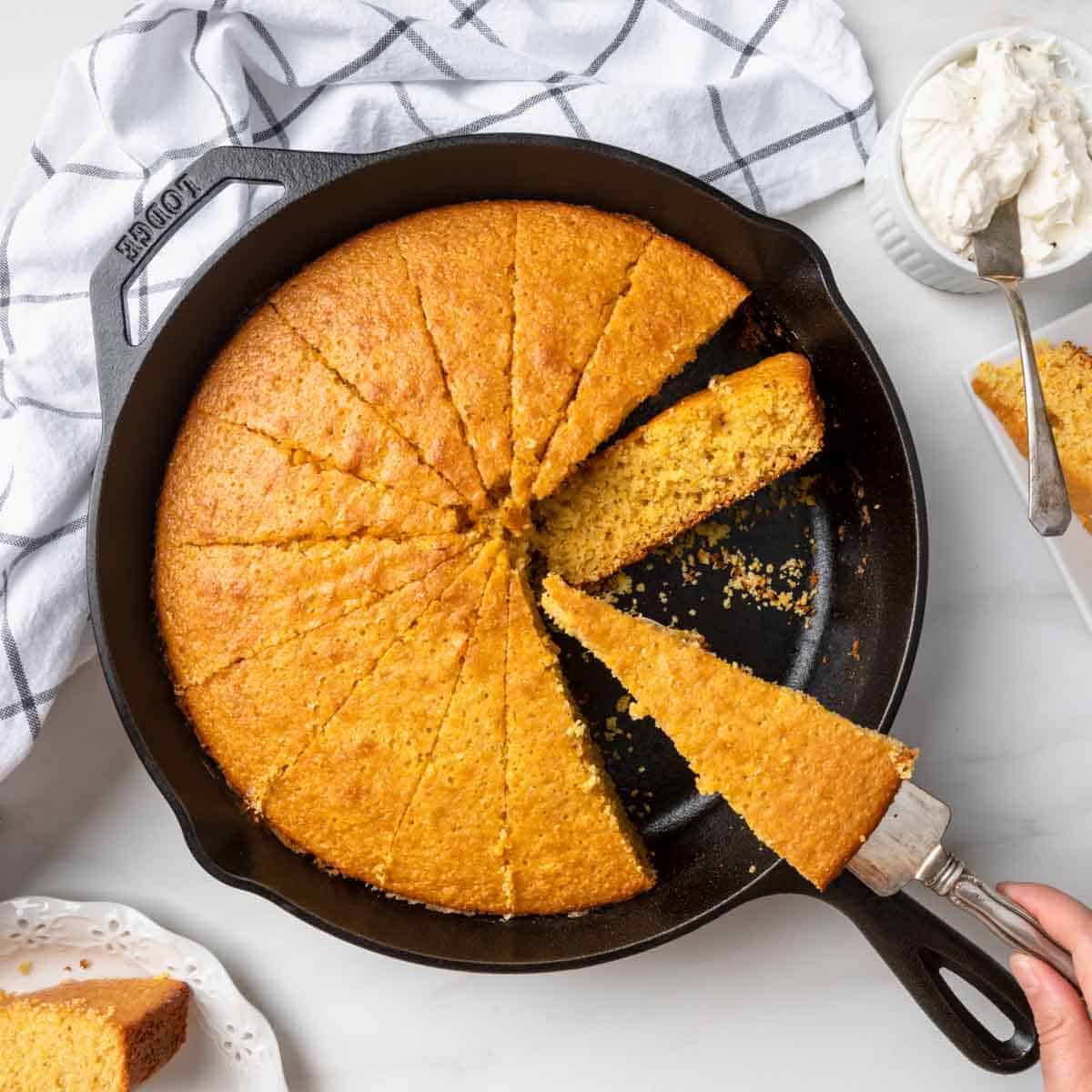 Sweet skillet cornbread in a cast iron pan with a piece being removed. 