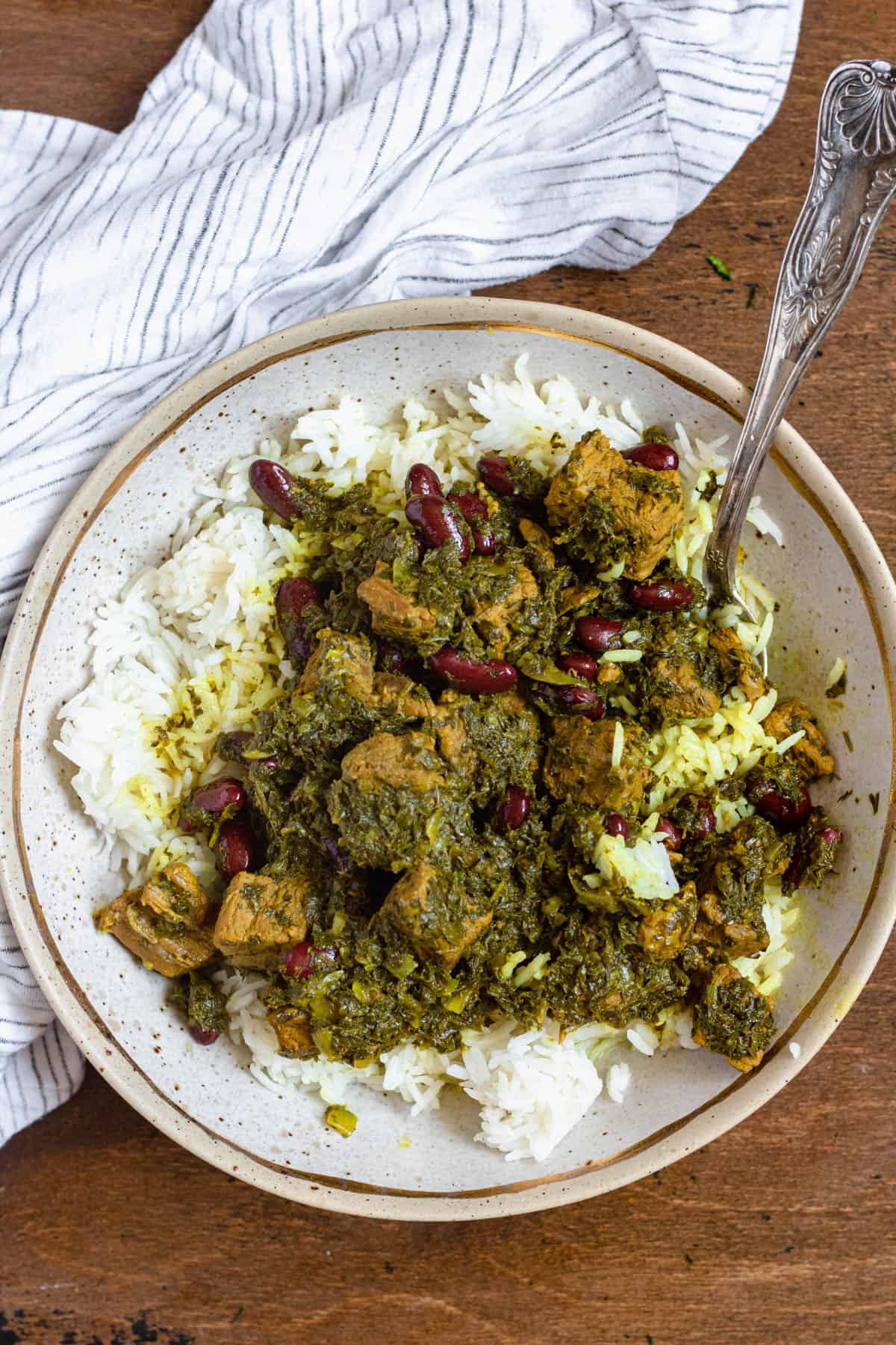 Seasoned stew meat served over basmati rice on a plate with a spoon known as ghormeh sabzi. 