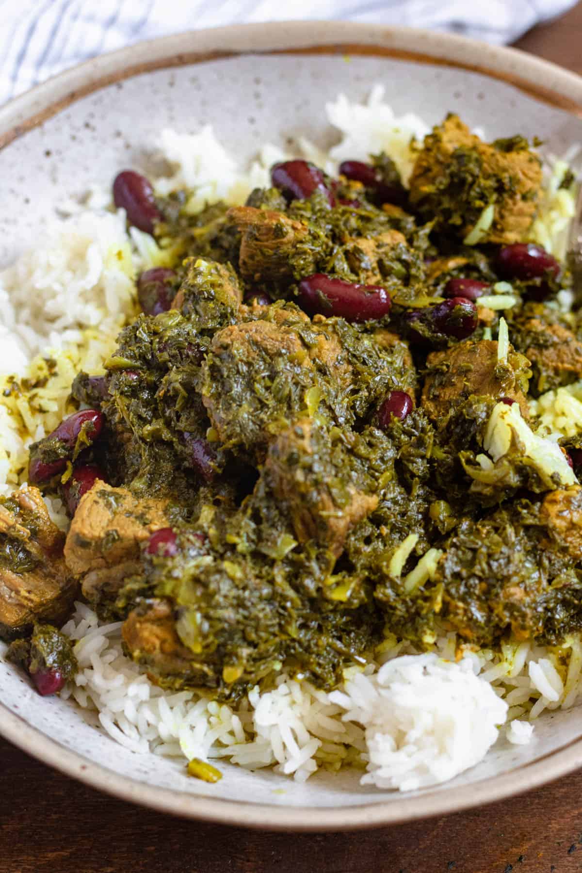 Plate of ghormeh sabzi served over a plate of rice. 