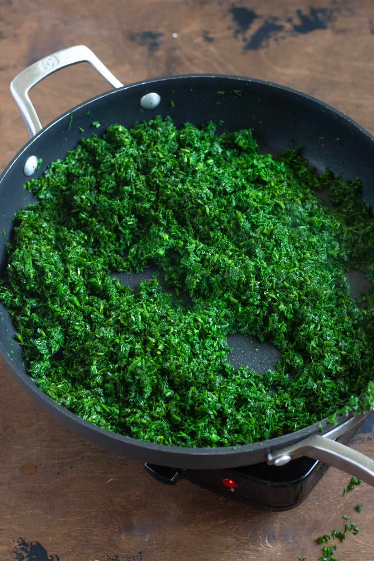 Pureed fresh herbs added to a frying pan for preparing ghormeh sabzi. 