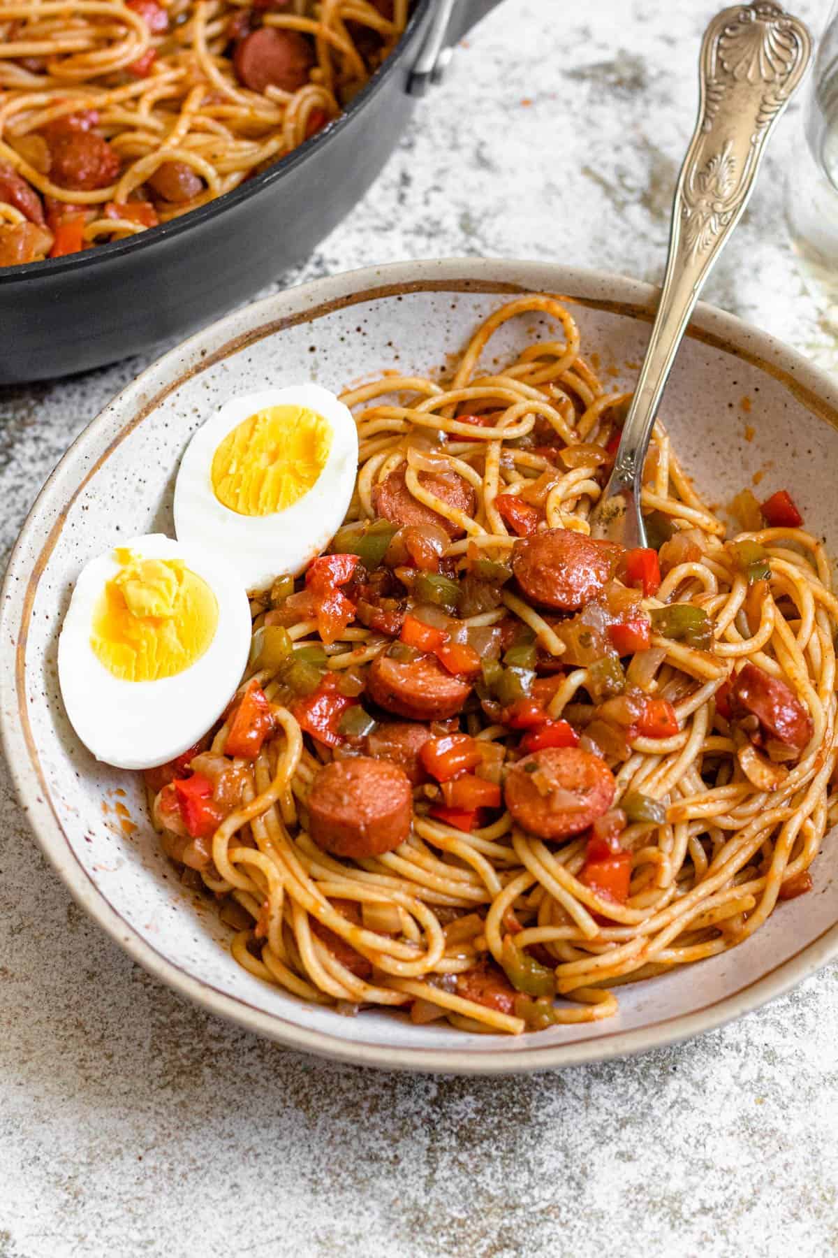 Plate of Haitian spaghetti with a boiled egg cut in half on the plate. 