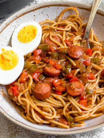 A bowl of Haitian Spaghetti with hot dogs and hard boiled eggs also in the bowl.