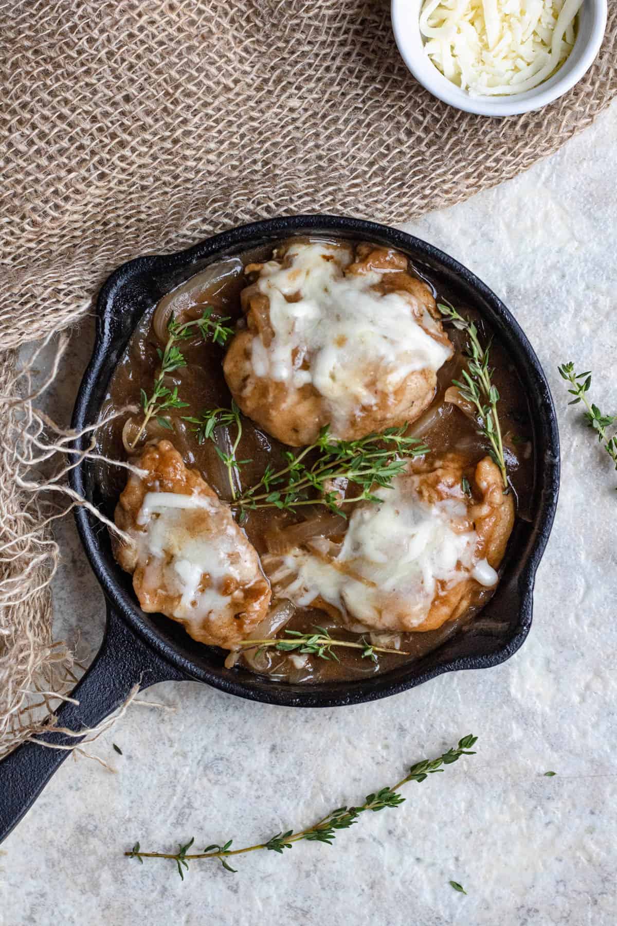 Cast iron pan with french onion chicken and cheese melted on top with fresh herbs garnished on top. 