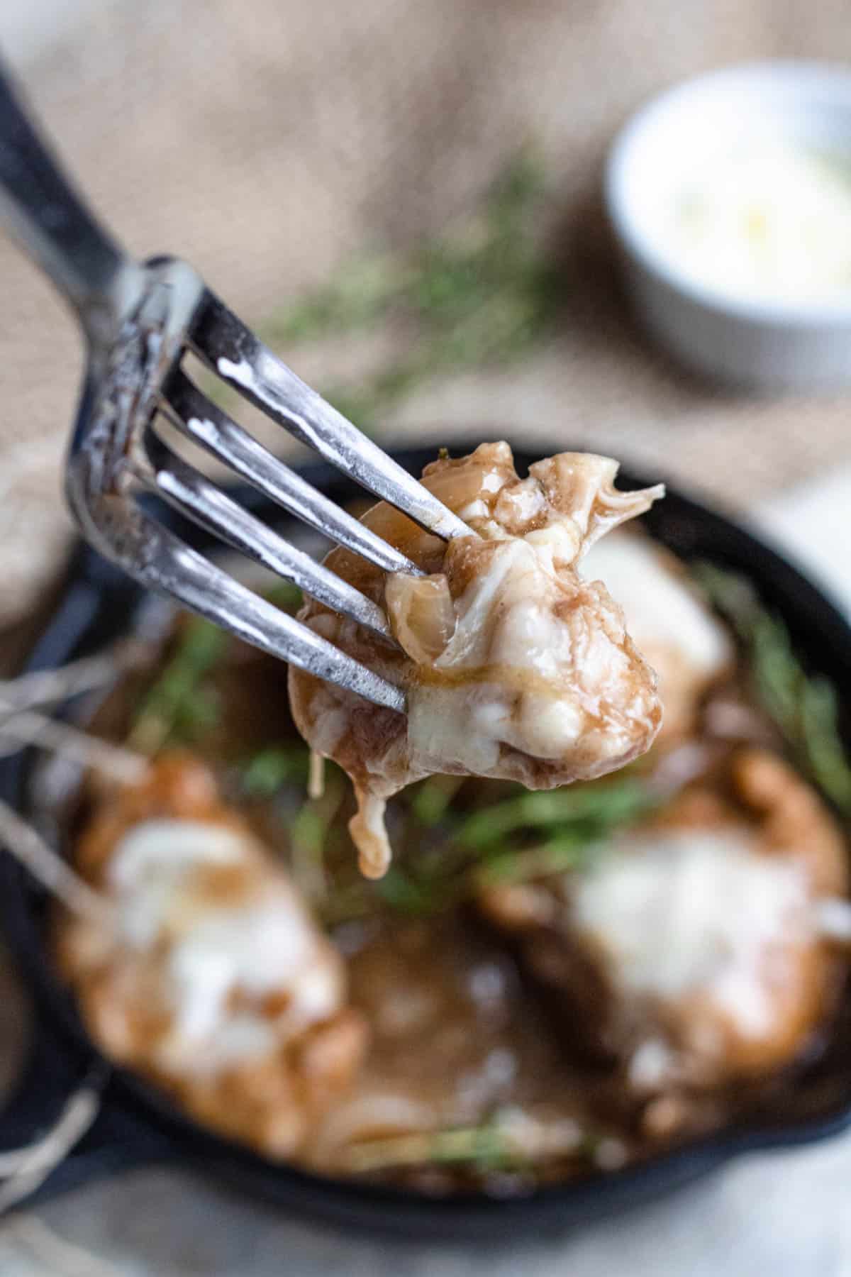 Bite of cheesy french onion chicken on a fork up close. 