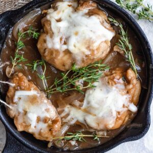 French onion chicken in a cast iron skillet topped with cheese and sitting next to sprigs of thyme.