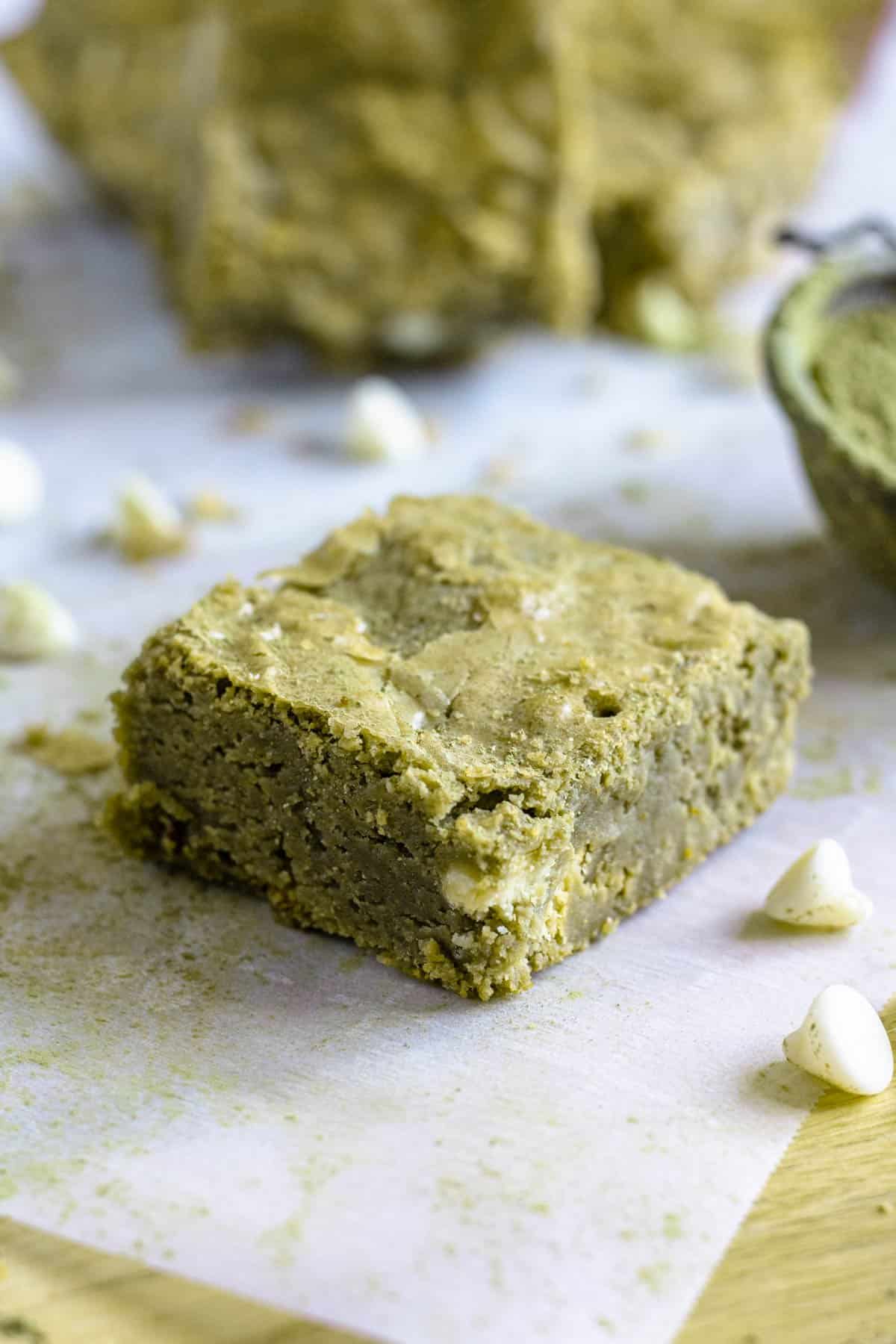 Matcha brownie on parchment paper surrounded by white chocolate chips. 