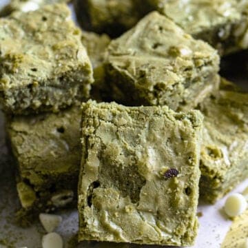 A pile of matcha brownies with white chocolate chips, sprinkled with matcha powder.