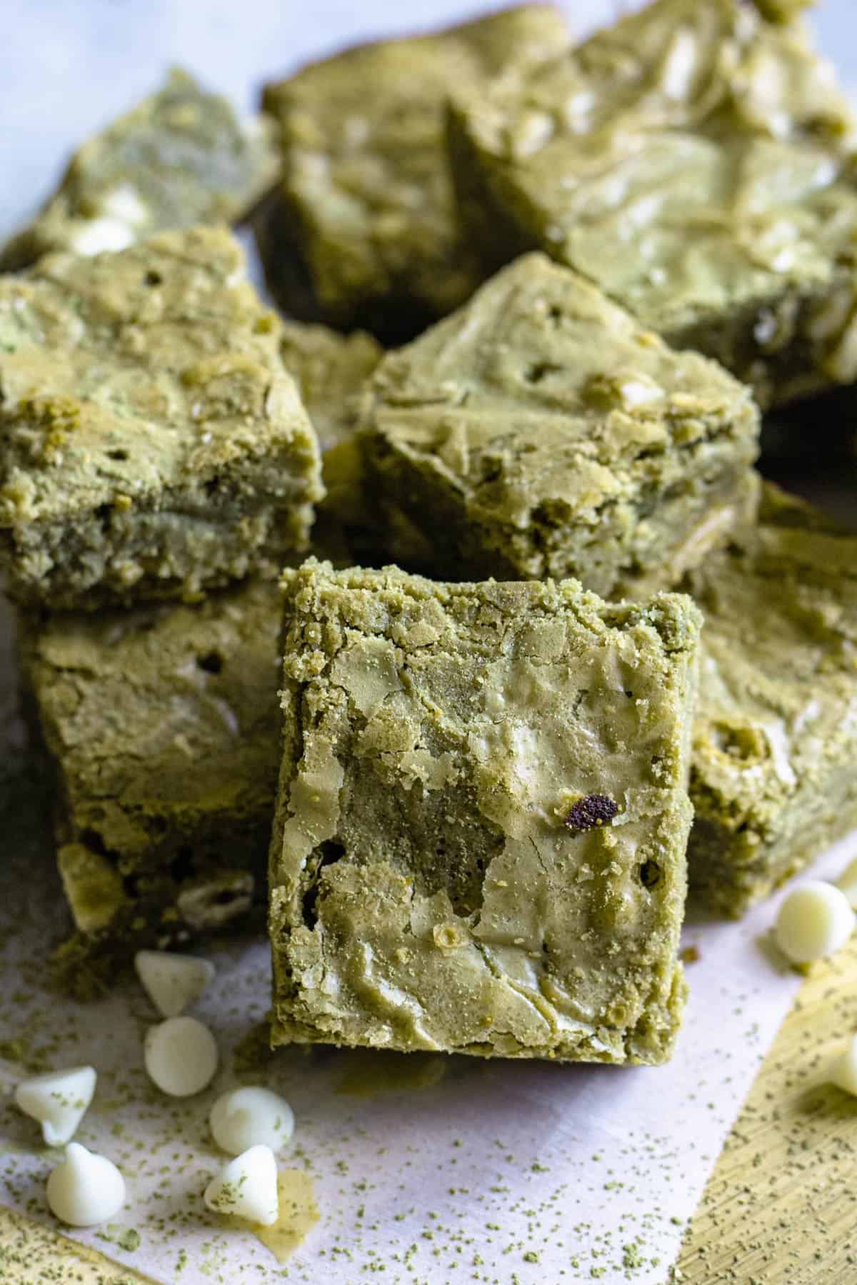 Square cut matcha brownies stacked together with white chocolate chips laying around it. 