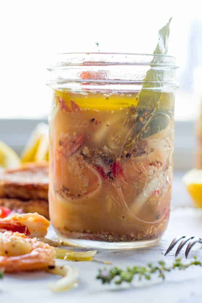 Pickled shrimp in a glass jar with a couple shrimp laying in front of the jar. 