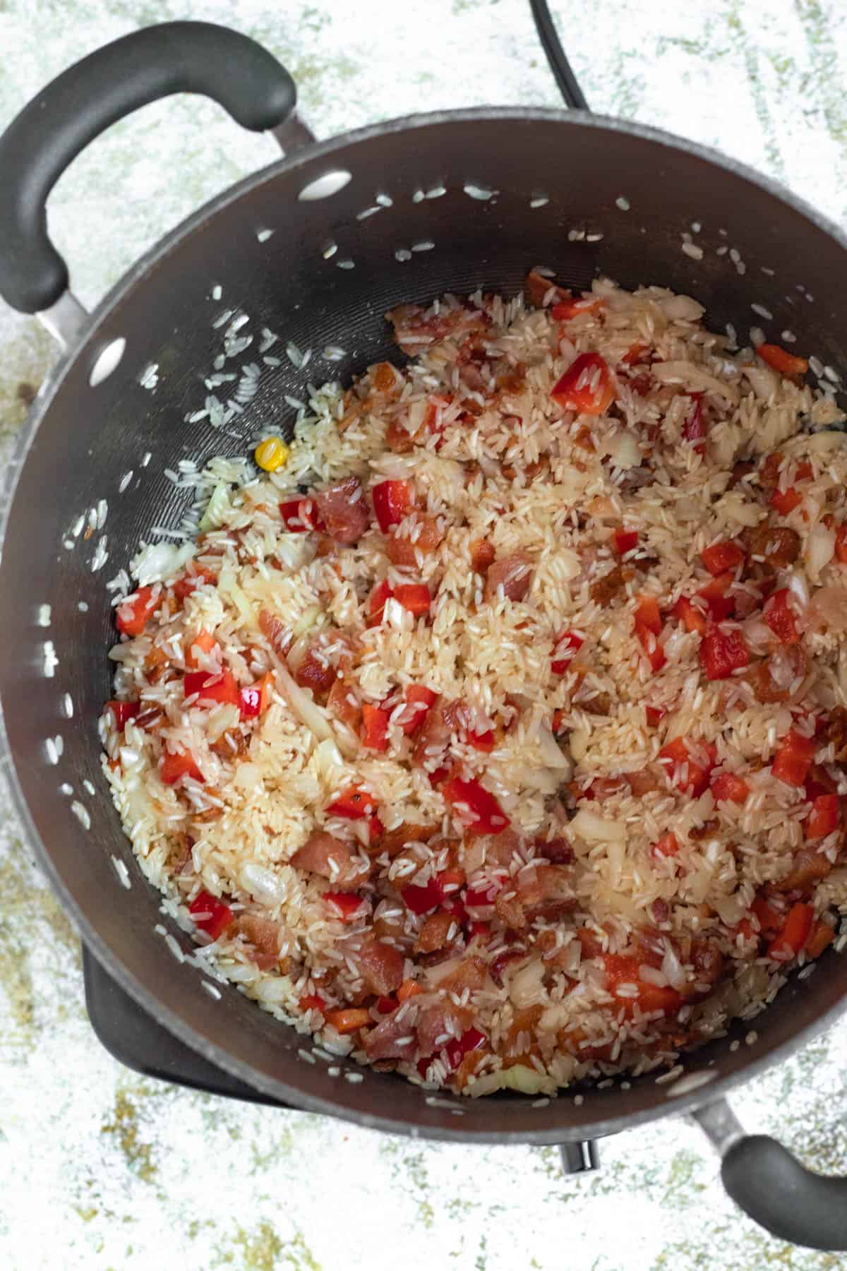 Rice added to the bacon in a pan. 
