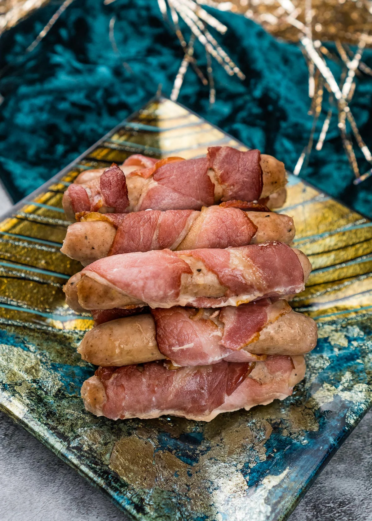 Bacon wrapped sausages on a small plate. 