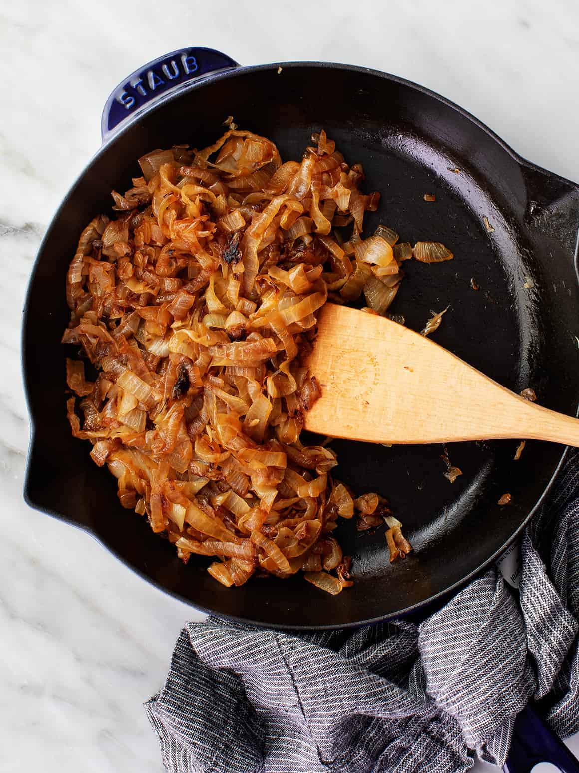 A wooden spoon stirring caramelized onions in a cast iron skillet. 