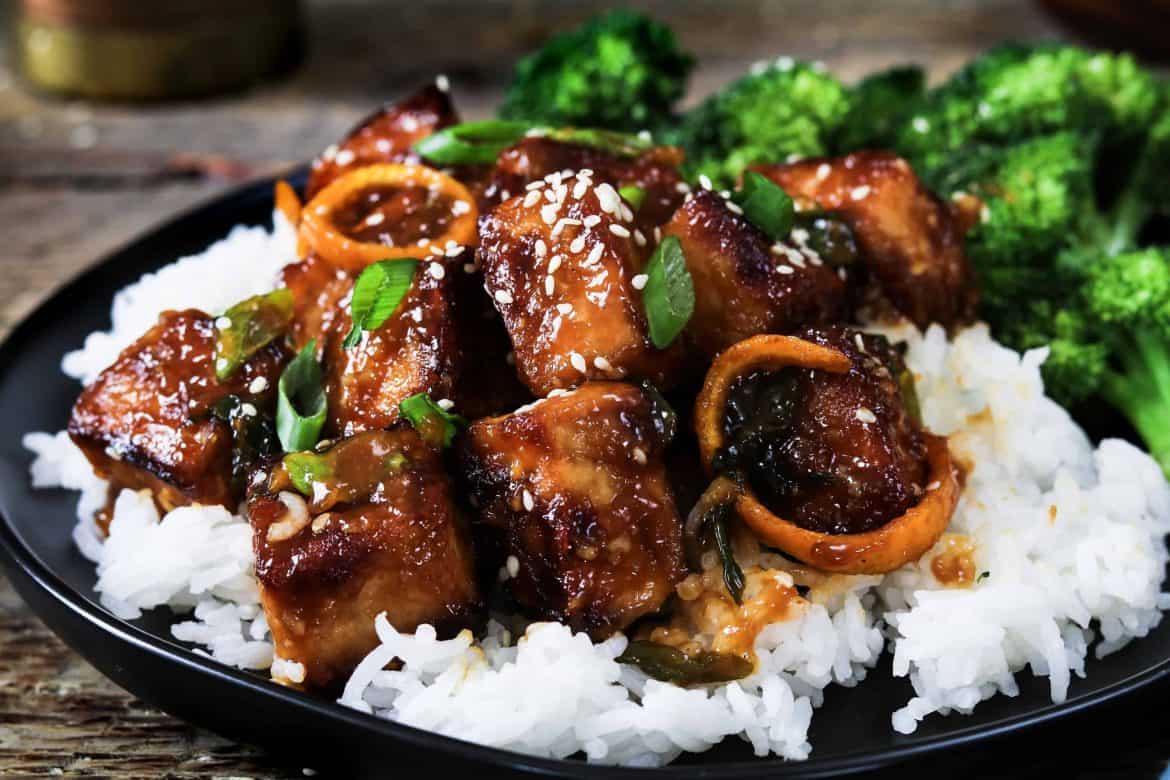 General Tso's tofu served over a bed of white rice on a black plate. 