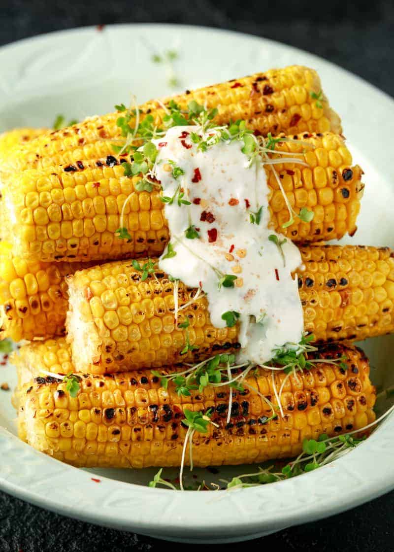 Several pieces of Grilled corn on the cob on a plate with a seasoning and aioli sauce dripping down the side. 