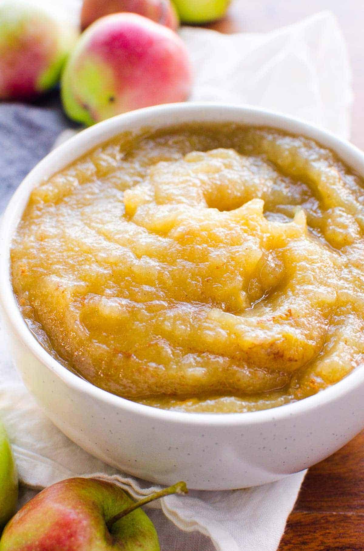 Instant Pot applesauce in a bowl with whole apples laying next to the bowl. 