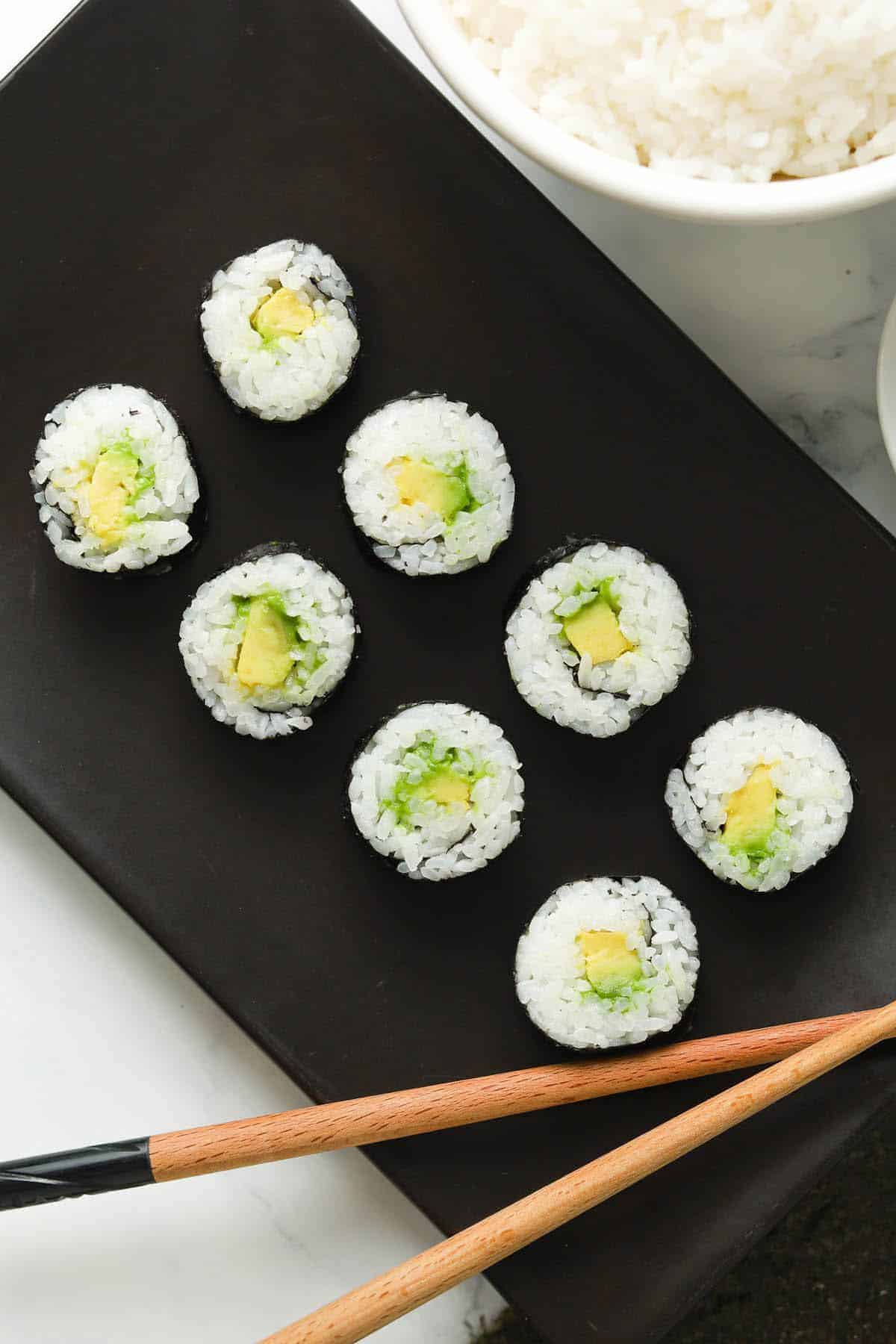 Avocado maki rolls served on a black rectangular platter. 