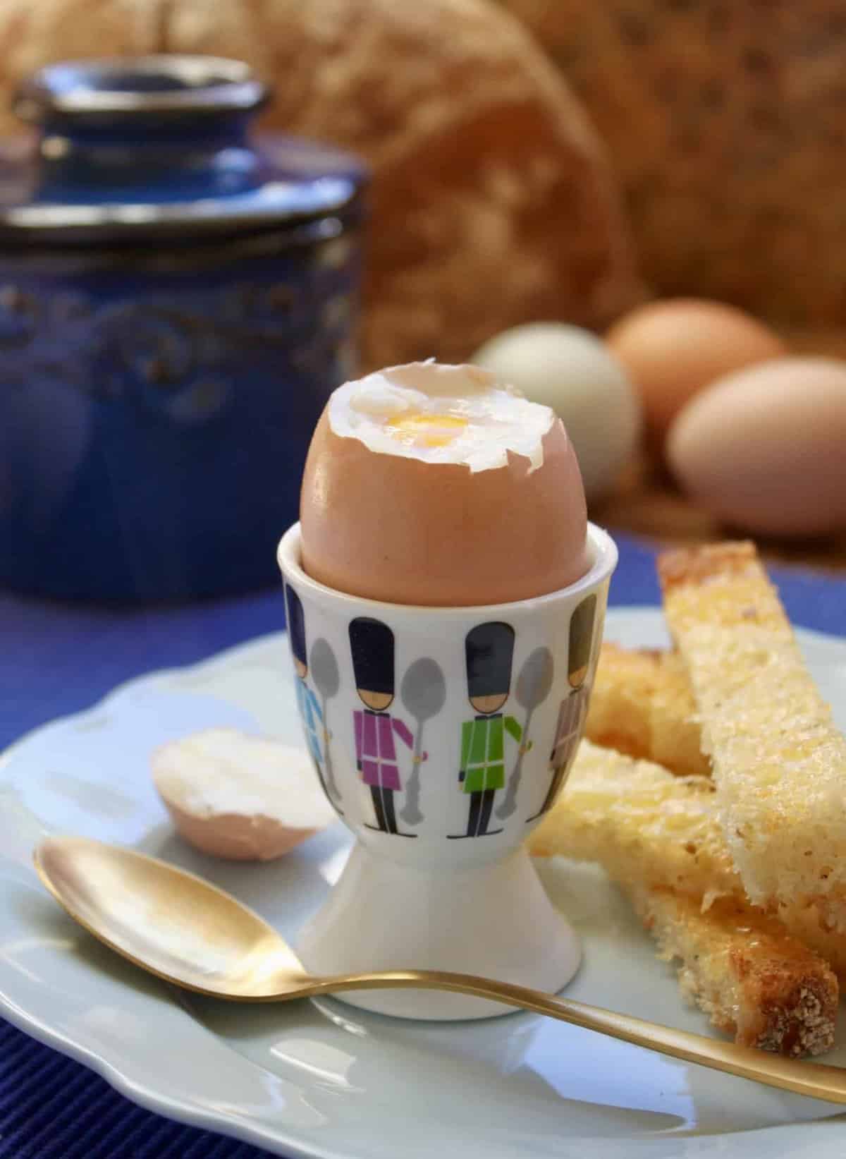 A soft boiled egg in a small container holding it upright with a spoon sitting in front of it. 