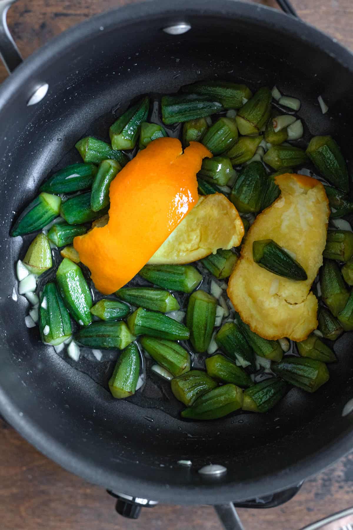 Cooking bamya by adding okra and the orange peel with the garlic and salt to the pot.