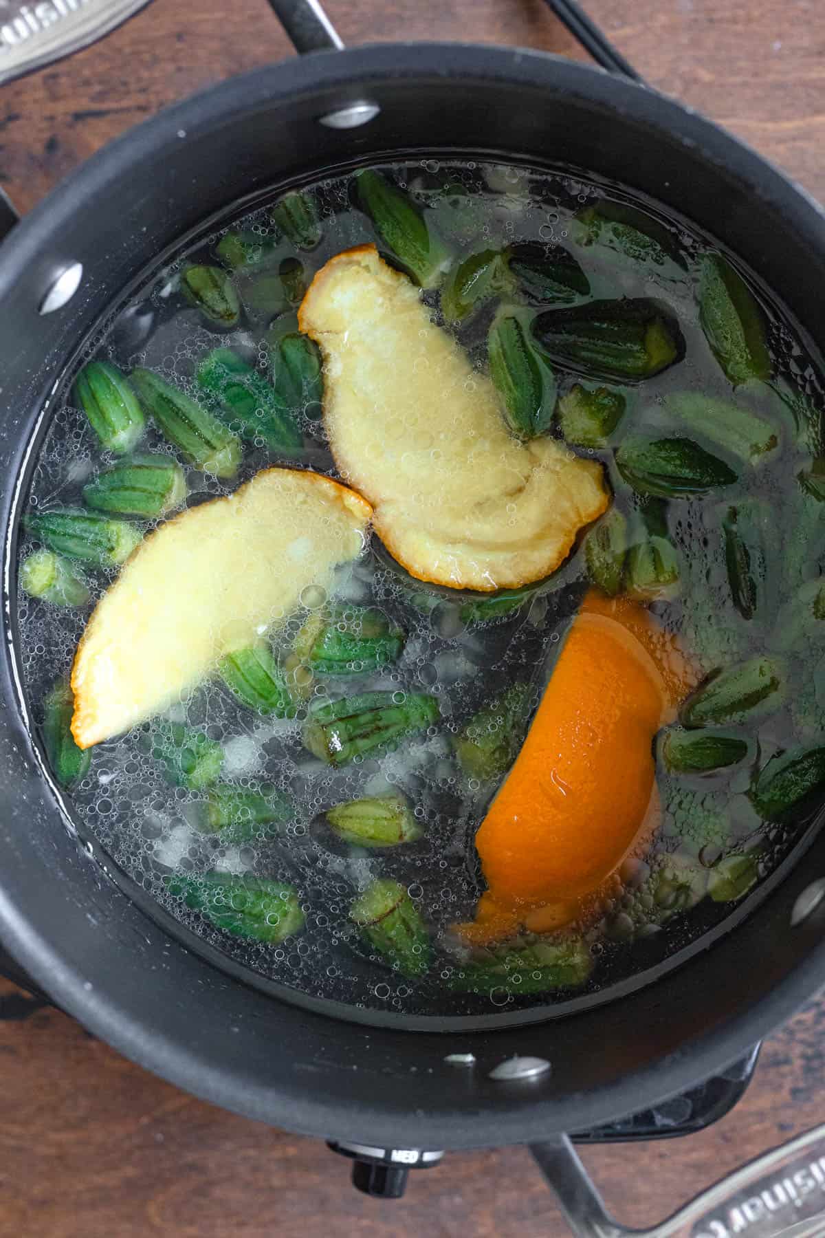Water added to the pot with okra and orange peel as you continue to prepare Bamya. 