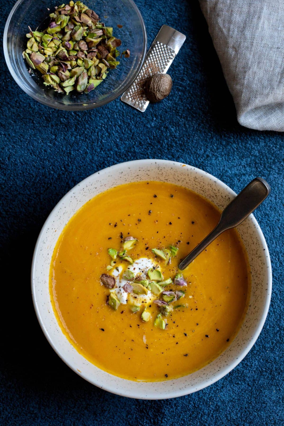 A bowl of carrot ginger soup garnished with creme and chopped pistachios. 