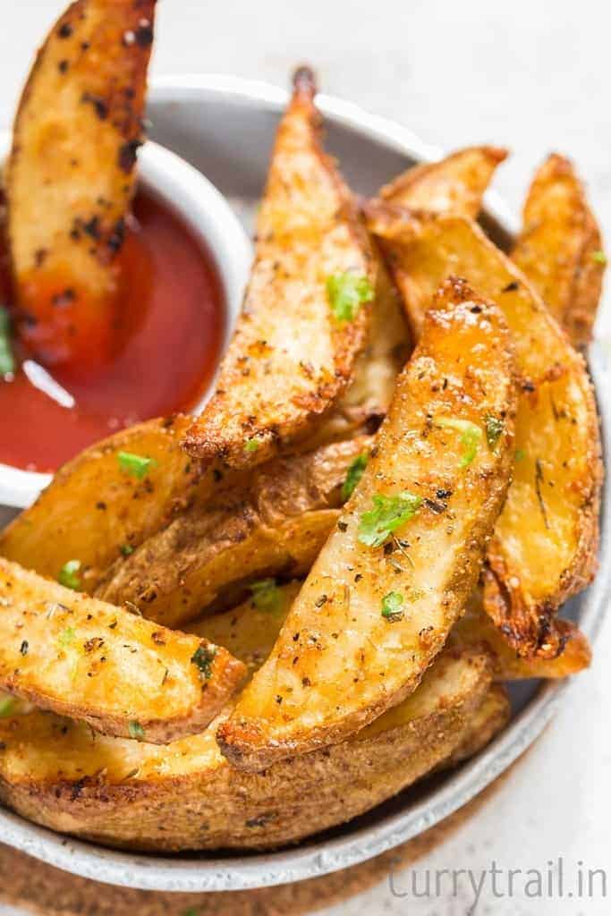 Garlic parmesan baked potato wedges in a small plate with a side of ketchup sauce. 